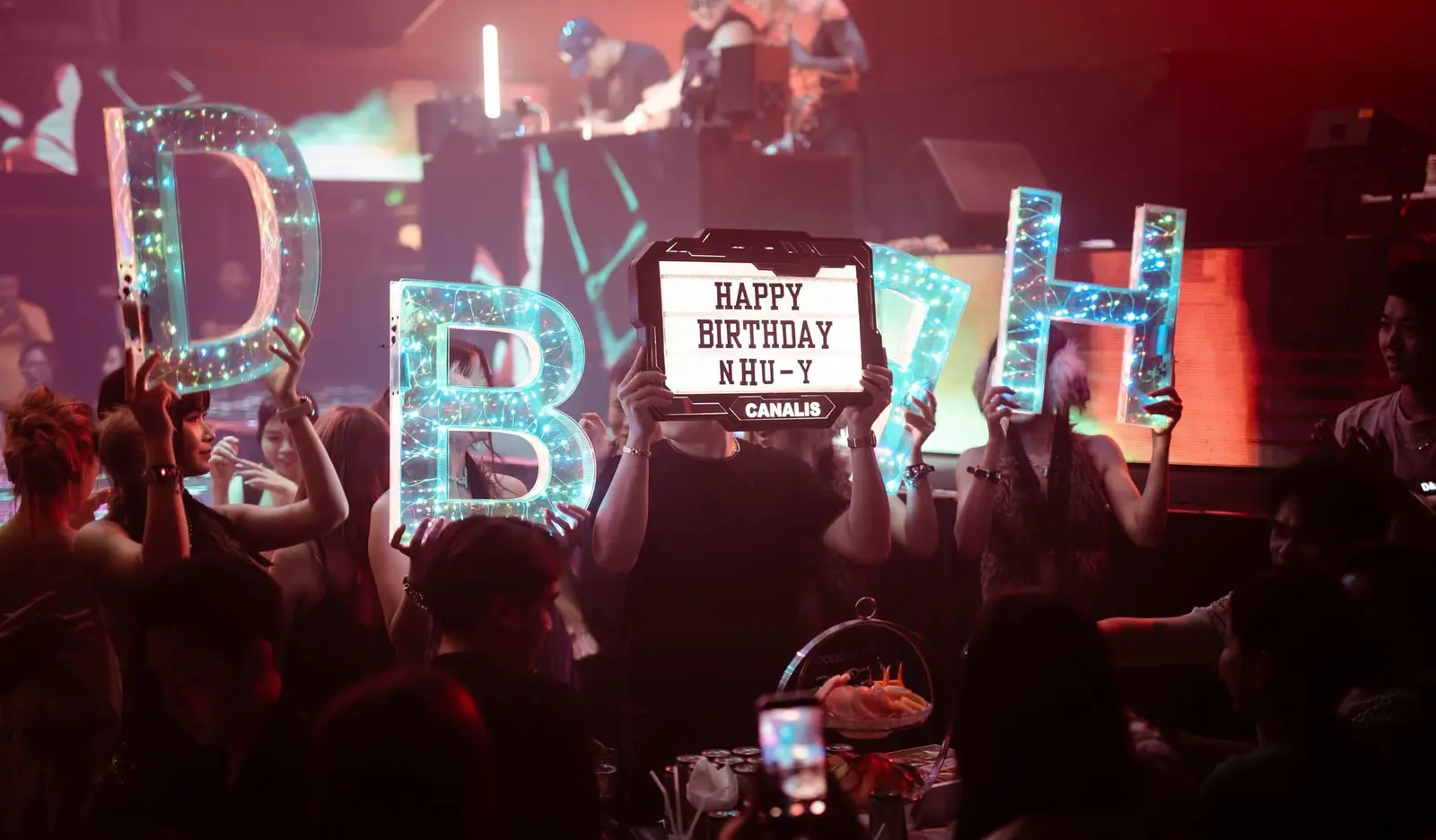 Bảng chữ phát sáng chúc mừng sinh nhật được giơ lên cạnh bốt DJ tại Canalis Club